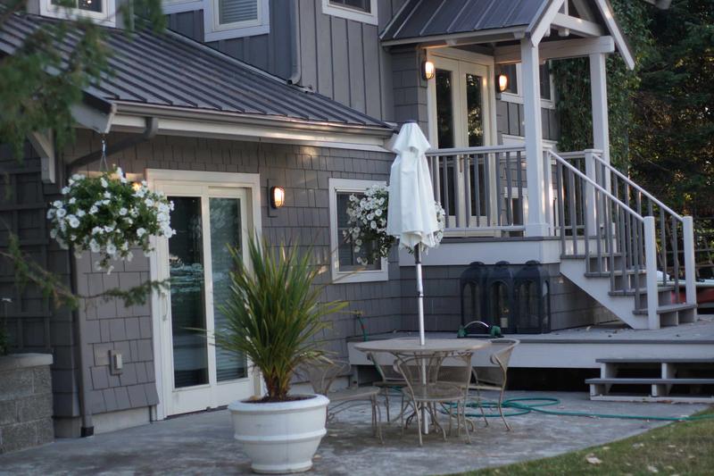 Back of a gray shingle-sided house with French doors, porch stairs and a deck with a patio table