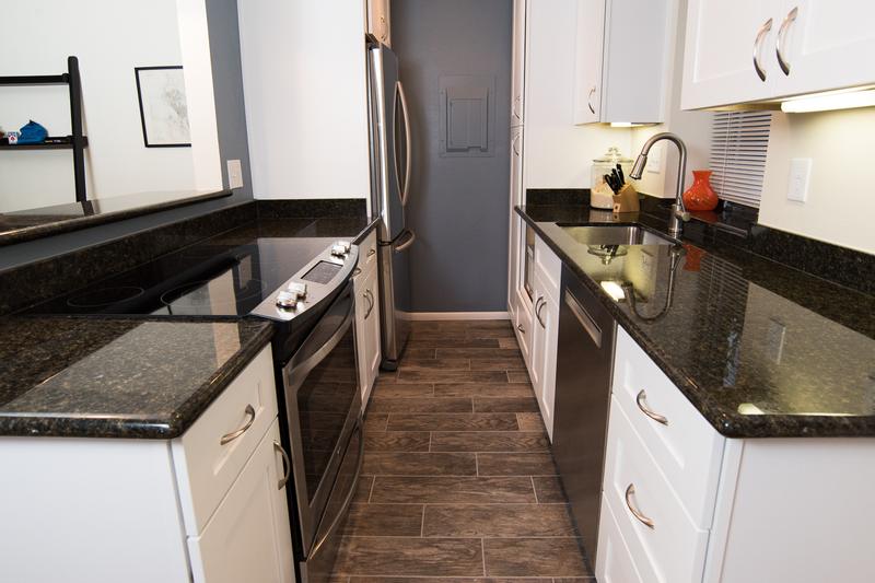 Galley kitchen with white cabinets, dark granite counters and a wood-look tile floor
