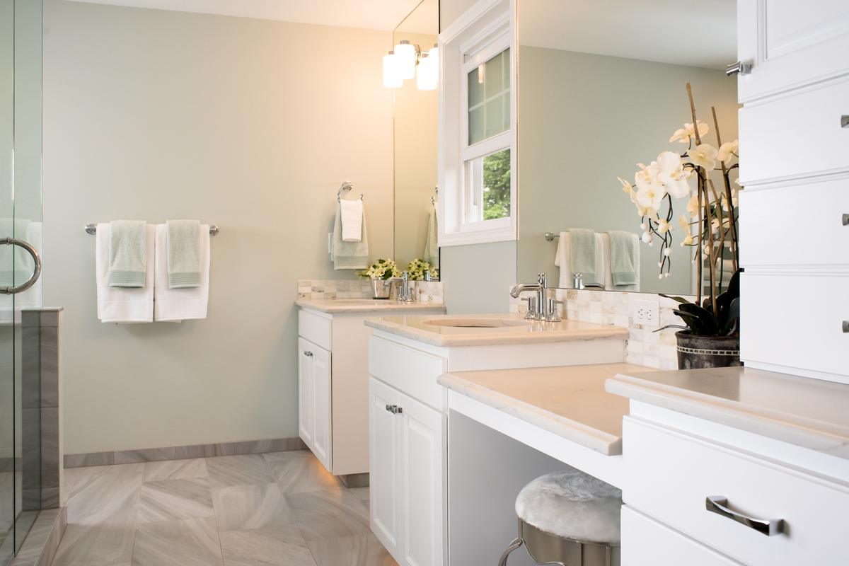 Bathroom with white vanity cabinets, a sit-down makeup counter and a glass shower