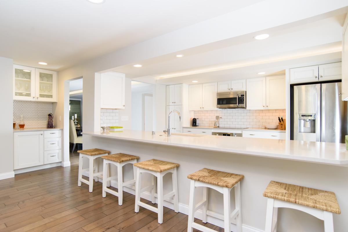 White kitchen with a long peninsula, woven-seat stools, a subway tile backsplash and wood floors