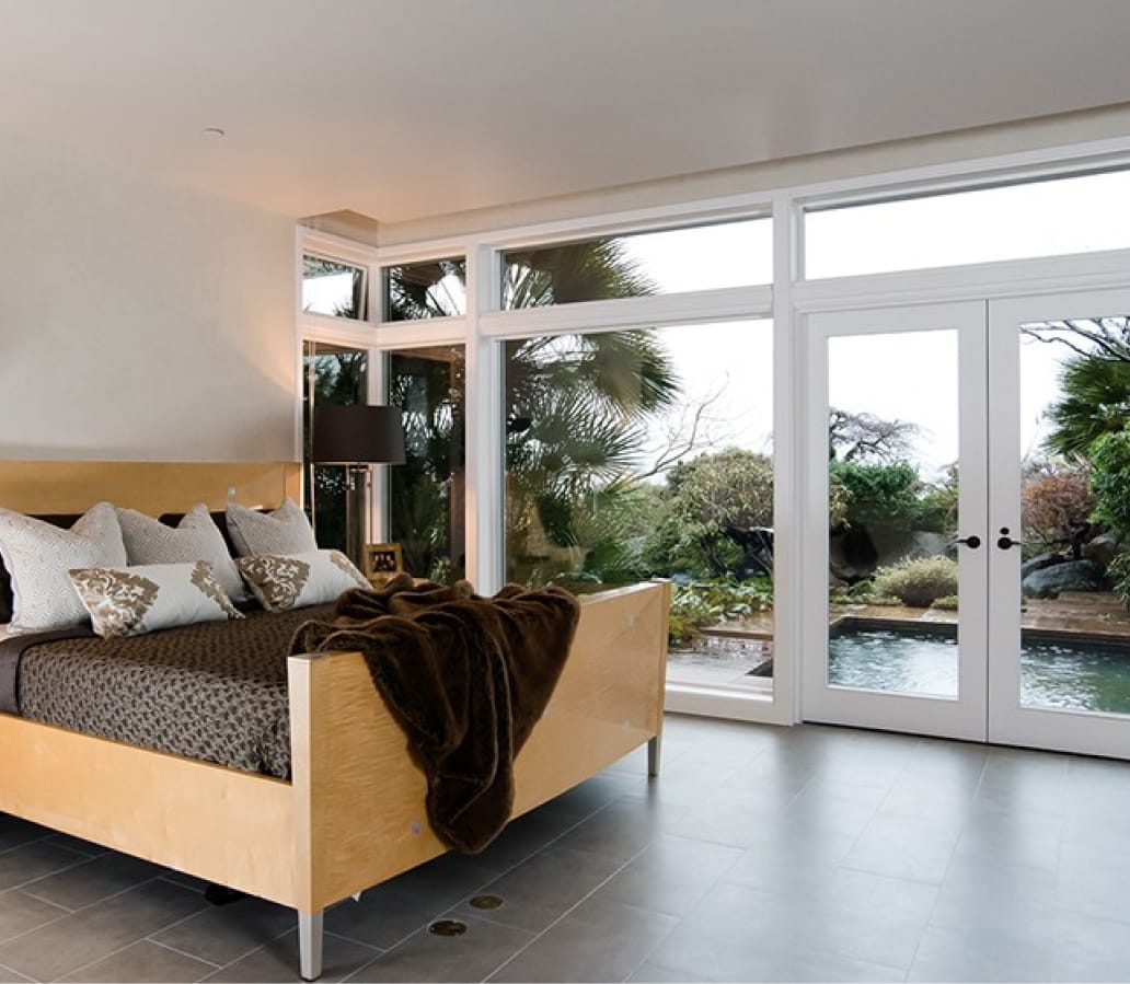 Renovated bedroom with stone tile floor and large floor to ceiling windows that look out to a water feature and plants