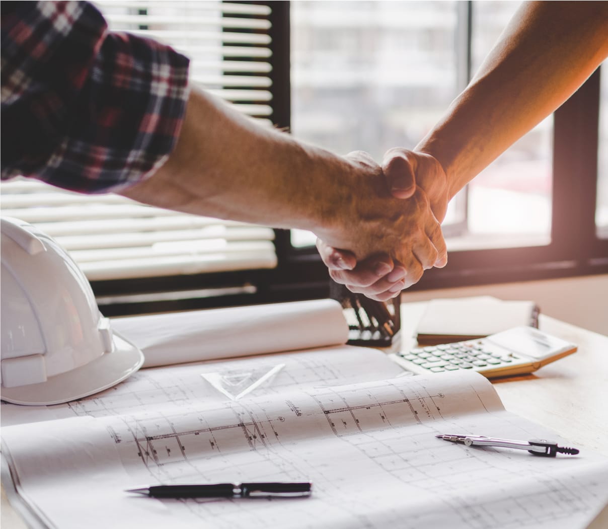 Two people shaking hands over a sheet of blueprints