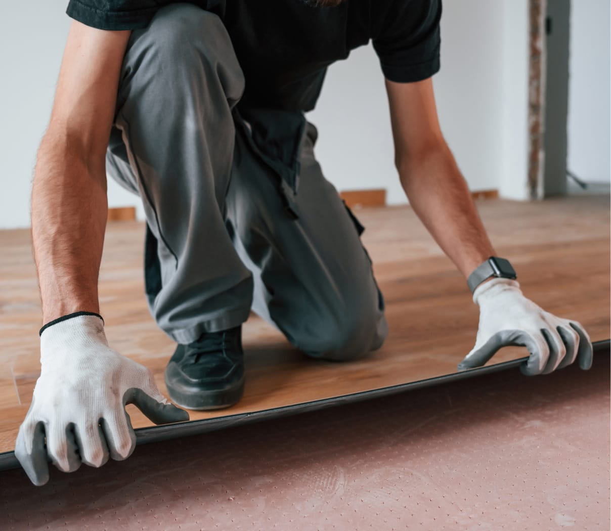 Worker laying brown laminate flooring in a home