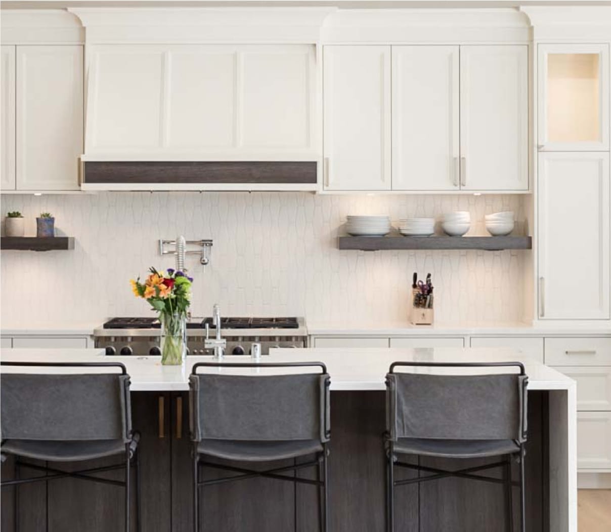 Remodeled kitchen with white cabinetry, white bar-height countertop and black stools