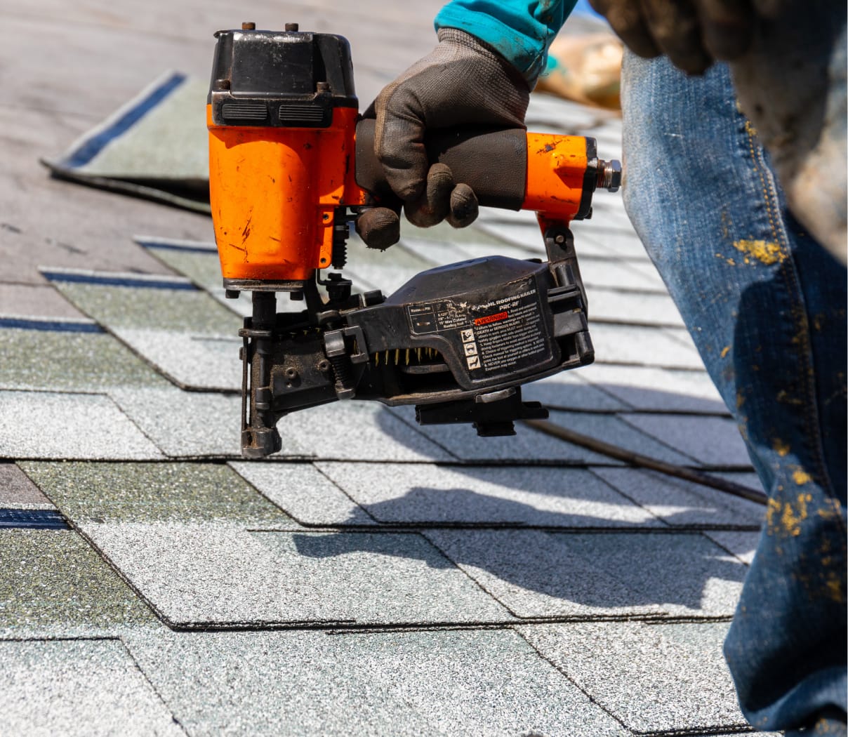 Worker using a nail gun to attach roof singles