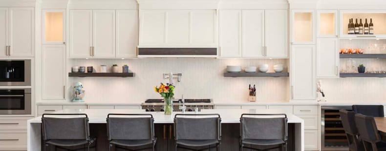 Remodeled kitchen with white cabinetry, white bar-height countertop and black stools